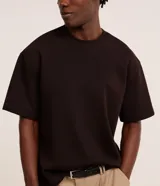 Remera masculina de corte boxy, color marrón oscuro, con cuello redondo y mangas cortas. Confeccionada en malla pesada con textura gomosa.