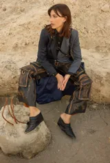 Botineta de gamuza azul marino con diseño drapeado, punta fina con puntera metálica y placa metálica decorativa en el lateral. Posee taco bajo cuadrado.