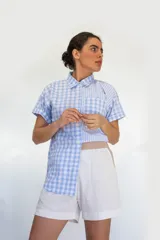 Camisa de manga corta con combinación de patrones a rayas y cuadros en tonos celeste y blanco, con bolsillo frontal aplicado y cierre de botones.