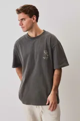 Remera marrón oversize de manga corta, con cuello redondo y pequeño estampado gráfico en el pecho.