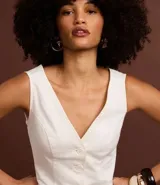 Chaleco femenino color blanco, sin mangas, con escote en V y abotonadura frontal. Presenta pences para un calce entallado y espalda descotada.