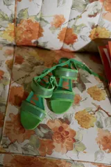 Sandalias de taco redondo de 6 cm, confeccionadas en gamuza verde con tiras frontales y de tobillo en material translúcido. Cuentan con cierre de pulsera al tobillo y plantilla de cuero.