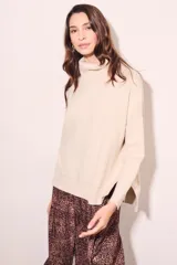 Polera color crema de algodón y elastano, con cuello alto, mangas largas y corte oversize con tajos laterales.