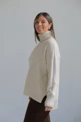 Polerón de cuello alto con diseño de rombos tejidos en relieve, mangas largas con puños acanalados y ruedo asimétrico con aberturas laterales.