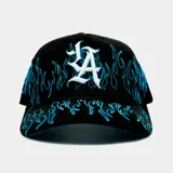 Gorro tipo trucker color negro con paneles frontales de tela y paneles traseros de malla. Presenta un diseño bordado de llamas en color azul que recorre la visera y los laterales, junto con un logo bordado en blanco en el frente.