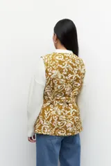 Chaleco capitoneado color crema con estampado floral en tonos marrones. Cuenta con cuello mao, cierre frontal con botones grandes y lazo en la misma tela para acentuar la cintura.