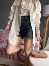 Camisa color crema de corte amplio, con cuello clásico, cierre frontal con botones a presión, mangas largas con puños abotonados y bolsillos de parche en el pecho.