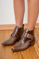 Botin de cuero negro con acabado brillante y detalle de solapa en cuero con textura de pelo, cierre con hebilla metálica lateral y punta fina.