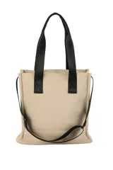 Bolso tipo tote color beige con doble asa superior negra y correa ajustable. Presenta un diseño estructurado con dos bolsillos frontales funcionales, uno con cierre y otro con solapa y broches a presión.