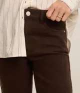 Pantalón slim de jean marrón, de cintura mediana con cierre frontal de cremallera y botón, bolsillos y trabillas para cinturón.