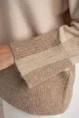 Sweater tipo polera de calce oversize, con diseño color block que combina tonos beige y marrón. Presenta cuello alto, mangas largas con puños acanalados y un panel inferior acanalado a juego.