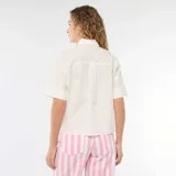 Camisa de corte holgado en color blanco, con cuello clásico, mangas cortas con dobladillo y cierre frontal con botones dorados en forma de estrella.