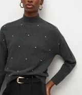 Suéter de punto color negro con cuello medio estructurado y mangas largas. Presenta un patrón geométrico sutil y aplicación de beads distribuidos por toda la parte frontal.