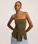 Top strapless de color verde oliva, ajustado al cuerpo en la parte superior y con un peplum asimétrico con corte en el bajo.