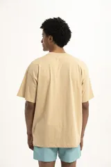 Remera color arena de corte holgado con bolsillo en el pecho y logo estampado en azul.