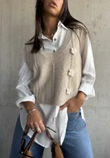 Chaleco de punto color beige con escote en V, diseño de trenzas verticales y tres flores tejidas en relieve.