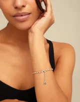 Pulsera de cadena compuesta por pequeños eslabones ovalados de acabado brillante, con cierre de mosquetón y dije colgante pequeño.