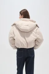 Campera puffer de color beige con cuello alto, capucha desmontable, cierre frontal y bolsillos laterales. Diseño de corte holgado con puños elásticos.
