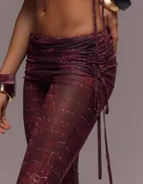 Conjunto de dos piezas compuesto por un top de manga corta con recortes, detalle metálico frontal y cuello tipo mao, y un pantalón de tiro bajo con corte flare. Ambas prendas presentan un estampado efecto piel de cocodrilo en tonos vino.