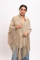 Poncho triangular tejido artesanalmente en telar manual, de lana merino color beige, con cuello alto y flecos largos en los bordes.