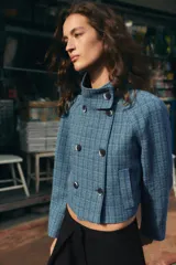Chaqueta corta de cuello subido y manga larga, con diseño de cuadros en tonos azules. Presenta cierre frontal cruzado con botones oscuros y bolsillos de vivo en el delantero.