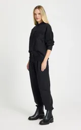 Pantalon tipo jogger de tiro alto, color negro, confeccionado en tejido de punto. Presenta una cinturilla elástica ancha con cordón ajustable y detalle de superposición de encaje en la parte delantera. Cuenta con bolsillos laterales ribeteados, perneras ligeramente holgadas y puños ajustados con elástico.