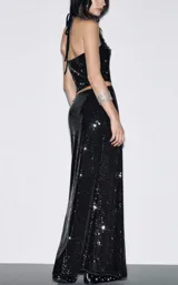 Conjunto de dos piezas compuesto por un top estilo halter con escote en V y una falda larga de corte recto, ambos confeccionados en tela con lentejuelas negras brillantes.