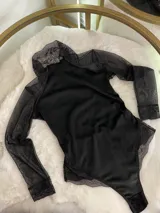 Body de manga larga confeccionado en una combinación de terciopelo, encaje y microtul. Presenta cuello alto, mangas de tul transparente con puños de encaje y detalles de encaje en la zona de la cadera.