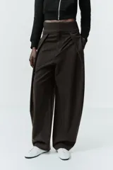 Pantalón de tiro alto con diseño tipo balloon, confeccionado en tela con estampado de rayas verticales. Presenta cintura ancha, pliegues frontales, bolsillos laterales y cierre frontal con cremallera, botón y ganchos metálicos.