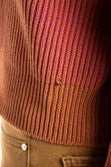 Campera tejida de algodón con diseño acanalado, cuello alto y cierre frontal completo. Presenta un patrón bicolor en tonos terracota y rosado, con puños y cintura elásticos.