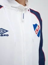 Campera deportiva Umbro del Club Nacional de Football, modelo Venti, para hombre. Diseño en color blanco con mangas azules y detalles de líneas rojas. Cuenta con capucha con cordón ajustable, cierre frontal y bolsillos. Presenta el logo de Umbro y el escudo del club bordados en el pecho.