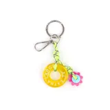 Llavero con argolla metálica y mosquetón, compuesto por un cordón de nylon verde neón con detalles negros, un dije circular de resina amarilla con la inscripción 'EXTRA LARGE' y un dije en forma de flor fucsia con centro celeste.