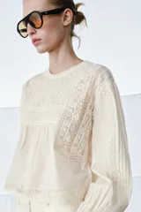 Camisa de algodón color crudo con cuello redondo y cierre de lazada en la espalda. Presenta mangas largas con puños, tablas y detalles de bordados y entredoses en el frente.