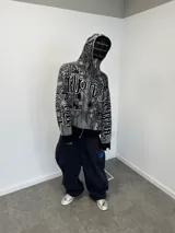 Buzo con cierre frontal completo, confeccionado en tejido de punto grueso de algodón. Presenta un diseño estampado integral con motivos gráficos y tipografía estilo gótico en tonos gris y negro, capucha integrada, puños y ruedo acanalados en color negro sólido.