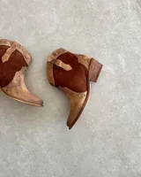 Botas texanas cortas de cuero vacuno color marrón con detalles de cuero marrón oscuro y tachas plateadas.