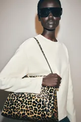Bolso de hombro confeccionado en piel con estampado animal print de leopardo y textura. Cuenta con compartimento interior con cremallera, asa larga de hombro y cierre mediante botón imantado.