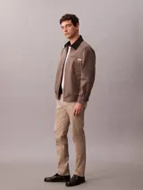 Pantalón chino de corte slim, confeccionado en tejido elástico de algodón orgánico. Presenta cierre de botón y cremallera, bolsillos laterales y bolsillos traseros ribeteados.