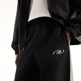 Pantalón New Balance de hombre, modelo Trackside, color negro con detalles laterales grises y logo impreso en la pierna. Cuenta con cintura elástica y diseño deportivo.