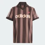 Camiseta de fútbol Adidas de manga corta, color marrón con diseño de rayas verticales oscuras. Presenta cuello polo con escote en V, el logo clásico de la marca bordado en el pecho junto con la inscripción "adidas" en gran tamaño al frente, y las franjas características de la marca en los hombros.