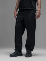 Pantalón cargo negro de corte oversize, confeccionado en microfibra elastizada. Presenta cintura elástica, bolsillos laterales y un bolsillo cargo con cierre de broche a presión. Incluye un sistema de elásticos con tancas en los tobillos para ajustar la apertura.