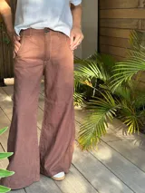 Pantalón marrón de lino y algodón, de tiro medio y pierna ancha, con bolsillos delanteros y traseros, pespuntes en contraste y remaches.