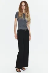 Pantalón de tiro bajo y corte recto, color marrón oscuro. Presenta bolsillos laterales, cierre frontal con cremallera y gancho metálico, y un cinturón integrado del mismo tejido con hebilla metálica.