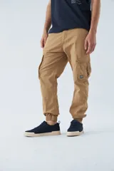 Pantalón cargo color beige, corte slim, con bolsillos laterales con botón, cierre con botón y puños en los tobillos.