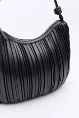 Cartera de hombro negra con diseño plisado vertical, asas largas con nudos decorativos y cierre de cremallera.