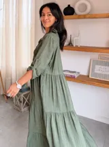 Vestido largo de estilo camisero en color azul, con cuello clásico, cierre frontal de botones y mangas tres cuartos con trabillas. Presenta un diseño de falda con cortes horizontales que le otorgan volumen y movimiento.