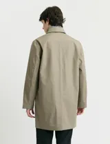 Gabardina clásica de corte recto, color beige, con cuello camisero, cierre frontal de botones y bolsillos laterales. Confeccionada en tejido técnico repelente al agua y al viento.