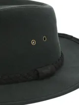 Sombrero de ala ancha verde oscuro, confeccionado en canvas engrasado con detalles de ojales metálicos laterales y cinta trenzada oscura alrededor de la copa.