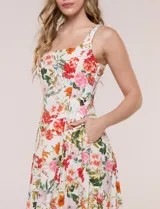 Vestido midi evasé de lino estampado con diseño floral multicolor sobre base beige. Cuenta con escote cuadrado, tirantes anchos y cierre invisible en la espalda.