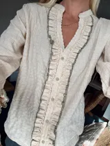 Blusa de manga larga color rosa pálido con textura arrugada, cuello mao y abertura frontal con botones. Presenta volados con ribete en contraste a lo largo de la botonera.