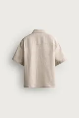 Camisa de lino color blanco, con ajuste relajado, cuello bowling, manga corta y cierre frontal con botones.